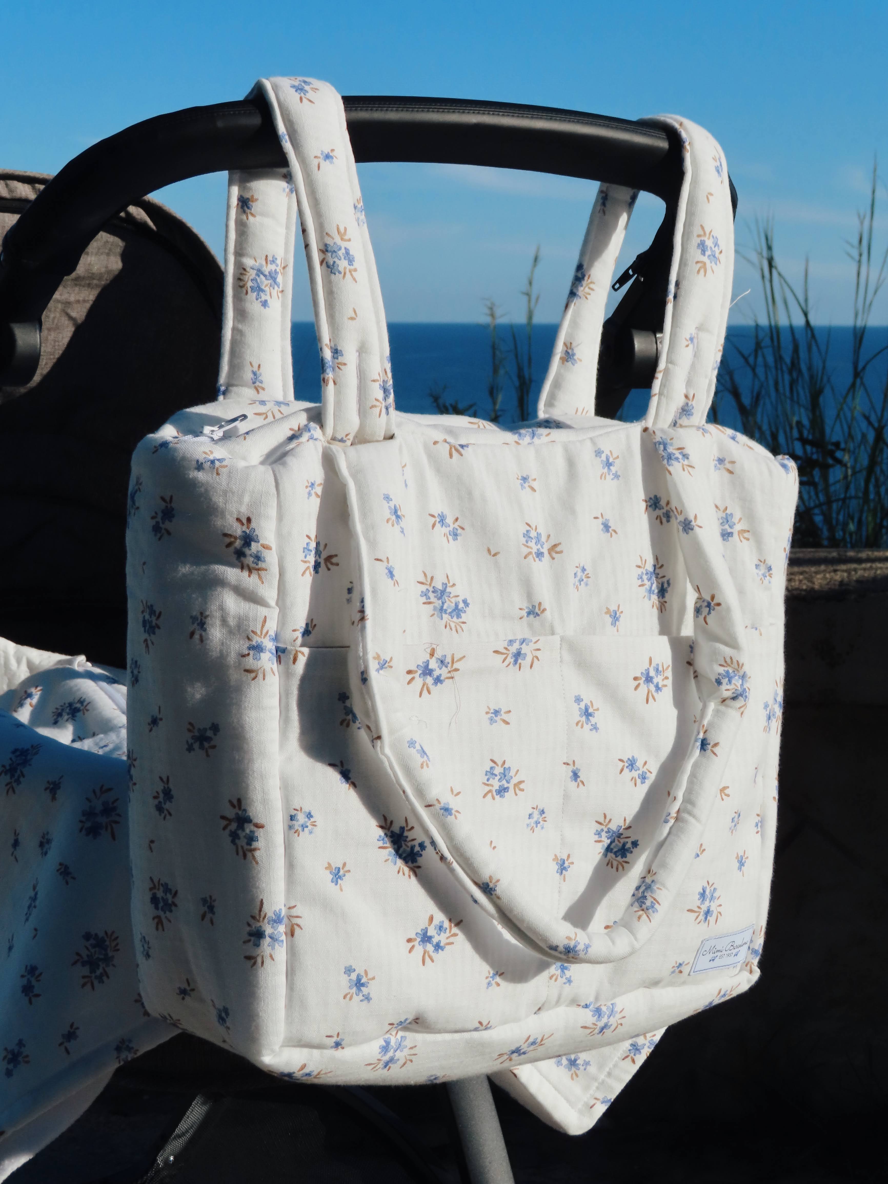 Floral-patterned baby carrier with a blue sky and ocean background
