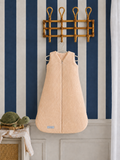 Beige baby sleeping bag hanging on a hook against a striped wall.