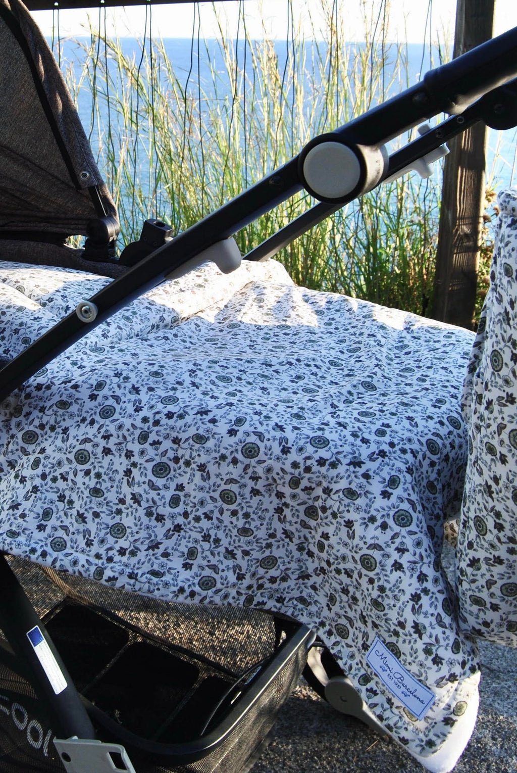A baby blanket with a seville print covering a stroller, displayed outdoors.