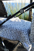 A baby blanket with a seville print covering a stroller, displayed outdoors.