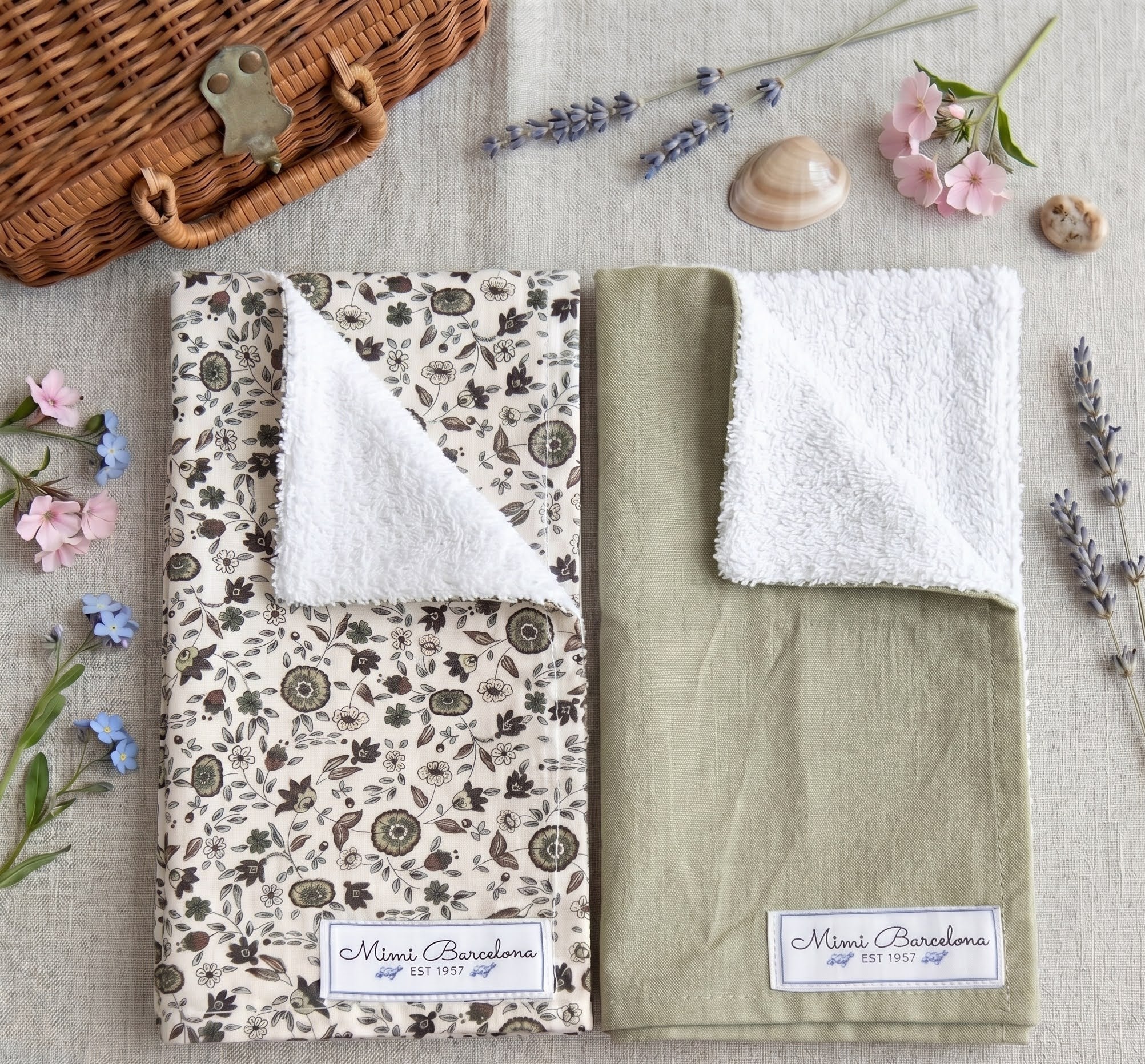 Two foldedbaby muslins, one with a floral pattern and the other green, on a textured surface with flowers and a wicker basket.